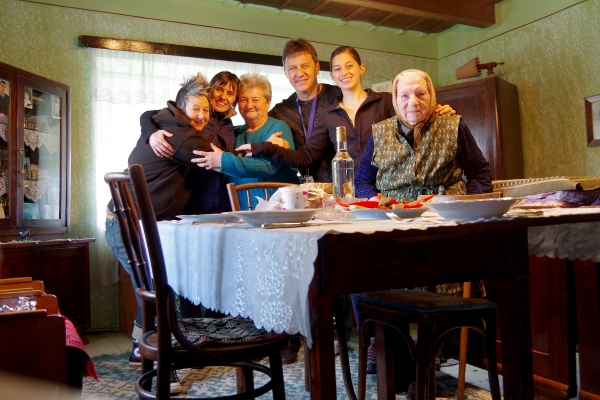 Spike visiting with her second cousins Béla and Csilla in Transylvania with their mother, grandmother, and Csilla’s daughter, all behind a wooden table with a white lace tablecloth.